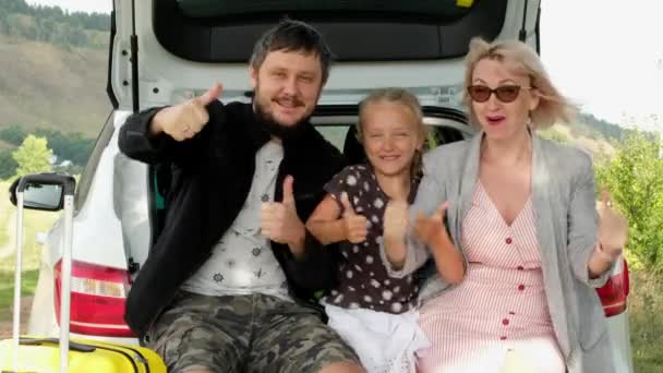Pappa, mamma och dotter visar tummen upp sittande i bagageluckan. Familjer med barn reser med bil. — Stockvideo