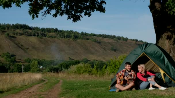 Mężczyzna i kobieta śpiewają piosenkę z gitarą siedzącą w namiocie. Rodzina jest na kempingu.. — Wideo stockowe