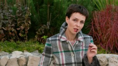 Paltolu modern kadın portresi parkta gözlük takıyor. Kadın kameraya bakıyor..