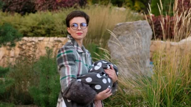 Mulher bonita em óculos embala um bebê em seus braços no parque. — Vídeo de Stock