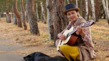 Parkta akustik gitar çalan şapkalı güzel bir kadın. Sokak müzisyeni bir şarkı söyler ve para ister..
