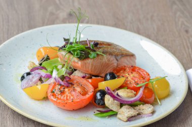 Somon bifteği ve beyaz tabakta sebze salatası.