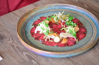 Bir restoran ortamında sade bir tabakta servis edilen sığır eti carpaccio yakın plan, taze malzemeler ve zarif Avrupa mutfağı sunumu.