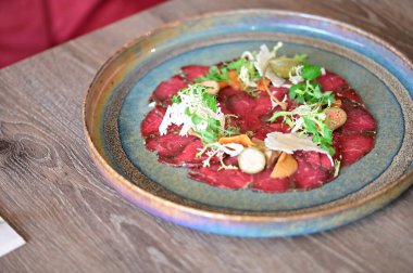 Bir restoran ortamında sade bir tabakta servis edilen sığır eti carpaccio yakın plan, taze malzemeler ve zarif Avrupa mutfağı sunumu.