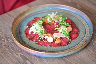 Bir restoran ortamında sade bir tabakta servis edilen sığır eti carpaccio yakın plan, taze malzemeler ve zarif Avrupa mutfağı sunumu.