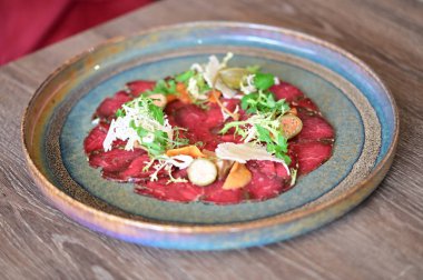 Bir restoran ortamında sade bir tabakta servis edilen sığır eti carpaccio yakın plan, taze malzemeler ve zarif Avrupa mutfağı sunumu.