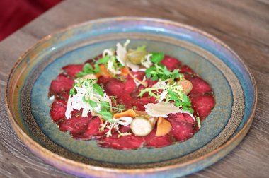 Bir restoran ortamında sade bir tabakta servis edilen sığır eti carpaccio yakın plan, taze malzemeler ve zarif Avrupa mutfağı sunumu.