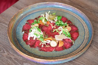 Bir restoran ortamında sade bir tabakta servis edilen sığır eti carpaccio yakın plan, taze malzemeler ve zarif Avrupa mutfağı sunumu.