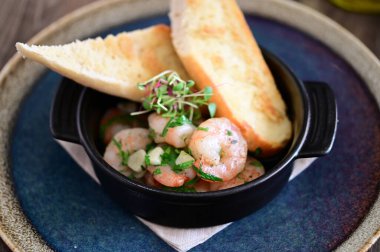 Bir gurme sunumunda canlı renkler ve deniz ürünlerinin dokularını vurgulayan baget ve taze otlarla servis edilen ızgara karidesin yakın çekimi.