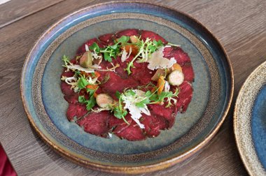 Biftek carpaccio ve taze salata ve parmesan talaşı. İnce dilimlenmiş çiğ et, zeytin yağıyla sulandırılmış, yeşil ile servis edilmiş.