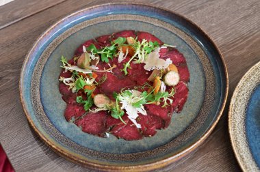 Biftek carpaccio ve taze salata ve parmesan talaşı. İnce dilimlenmiş çiğ et, zeytin yağıyla sulandırılmış, yeşil ile servis edilmiş.