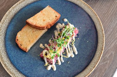 Yakın plan doğranmış dana tartı kremalı mayonez, taze otlar ve narin garnitürle servis edilir. Restoran tarzında zarif bir şekilde kaplanmış, etin detaylı dokusunu vurguluyor..