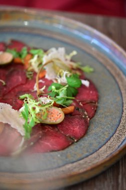 Biftek carpaccio ve taze salata ve parmesan talaşı. İnce dilimlenmiş çiğ et, zeytin yağıyla sulandırılmış, yeşil ile servis edilmiş.