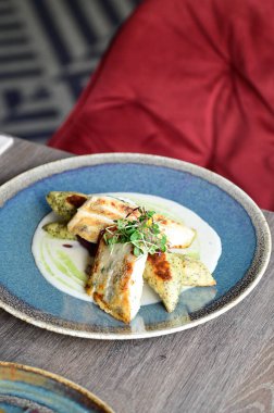 Köy tabaklarında patates gnocchi ile servis edilen kızarmış turna balığı, bir restoran ortamında ahşap bir masada sunuluyor. Arka planda, nefis, sağlıklı bir Avrupa mutfağı ve davetkar ve doğal bir sunum yer alıyor..