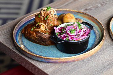 Kızarmış sığır kaburgası, yanında fırında patates ve otlu taze lahana salatası. Samimi ve lezzetli bir geleneksel yemek, otantik mutfak ve restoran fotoğrafçılığı için mükemmel bir kırsal yemek arka planında güzelce sunuluyor..