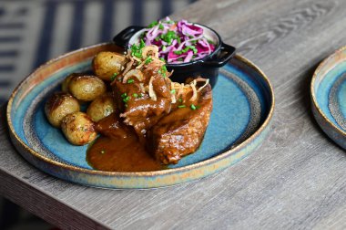 Kızarmış sığır kaburgası, yanında fırında patates ve otlu taze lahana salatası. Samimi ve lezzetli bir geleneksel yemek, otantik mutfak ve restoran fotoğrafçılığı için mükemmel bir kırsal yemek arka planında güzelce sunuluyor..