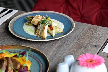 Köy tabaklarında patates gnocchi ile servis edilen kızarmış turna balığı, bir restoran ortamında ahşap bir masada sunuluyor. Arka planda, nefis, sağlıklı bir Avrupa mutfağı ve davetkar ve doğal bir sunum yer alıyor..