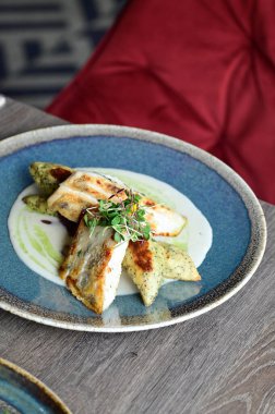 Köy tabaklarında patates gnocchi ile servis edilen kızarmış turna balığı, bir restoran ortamında ahşap bir masada sunuluyor. Arka planda, nefis, sağlıklı bir Avrupa mutfağı ve davetkar ve doğal bir sunum yer alıyor..