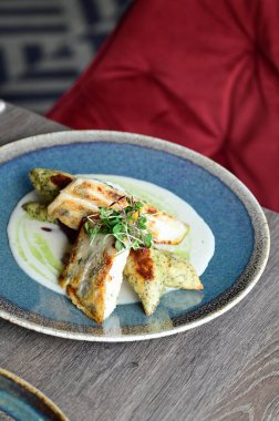 Köy tabaklarında patates gnocchi ile servis edilen kızarmış turna balığı, bir restoran ortamında ahşap bir masada sunuluyor. Arka planda, nefis, sağlıklı bir Avrupa mutfağı ve davetkar ve doğal bir sunum yer alıyor..