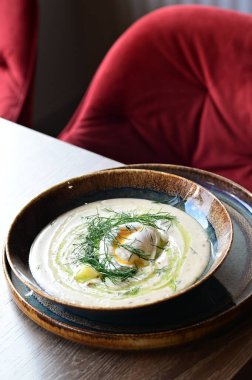 Dereotlu ve yumurtalı kremalı çorbaya yakın çekim. Bir restoranda, ahşap bir masada servis ediliyor. Orta Avrupa mutfağının sıcaklığını ve orijinalliğini yansıtan geleneksel ev yapımı bir yemek..