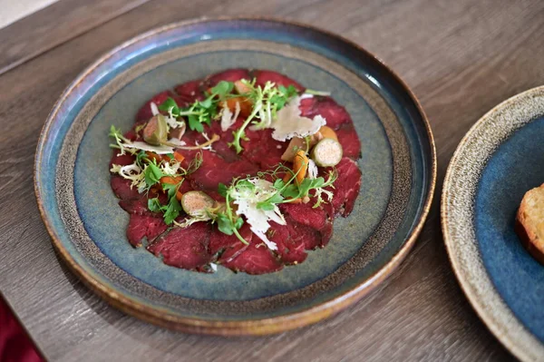 Biftek carpaccio ve taze salata ve parmesan talaşı. İnce dilimlenmiş çiğ et, zeytin yağıyla sulandırılmış, yeşil ile servis edilmiş.