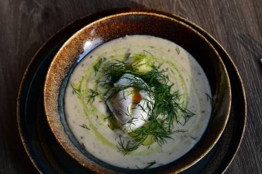 Bir restoranda servis edilen, dereotlu ve yumurtalı kremalı bir çorbanın yukarıdan aşağı görüntüsü. Geleneksel bir Avrupa yemeği, güzelce sunulmuş ve stil verilmiş, otantik tatlar sergileniyor ve ev yapımı yemekler rahatlatıcıydı..
