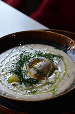 Ekşi kremalı çorba, yeşil soğan ve beyaz tabakta otlar..