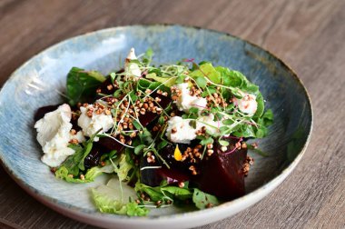 Kızarmış pancar kökü ve kremalı peynirli, yeşillik ve otlarla süslenmiş taze salatanın yakın görüntüsü. Renk ve lezzet dolu canlı ve sağlıklı bir yemek, modern mutfak, sağlıklı beslenme ve yemek fotoğrafçılığı için mükemmel..