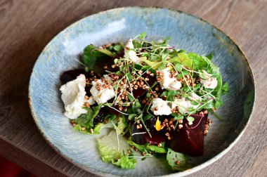 Kızarmış pancar kökü ve kremalı peynirli, yeşillik ve otlarla süslenmiş taze salatanın yakın görüntüsü. Renk ve lezzet dolu canlı ve sağlıklı bir yemek, modern mutfak, sağlıklı beslenme ve yemek fotoğrafçılığı için mükemmel..