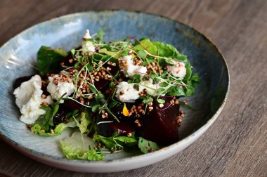 Kızarmış pancar kökü ve kremalı peynirli, yeşillik ve otlarla süslenmiş taze salatanın yakın görüntüsü. Renk ve lezzet dolu canlı ve sağlıklı bir yemek, modern mutfak, sağlıklı beslenme ve yemek fotoğrafçılığı için mükemmel..