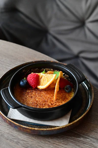 Gri arka planda taze meyvelerle servis edilen lezzetli tatlı crme brle 'ın yakın plan görüntüsü. Lezzetli bir karamelize kremalı tatlı, çıtır çıtır, güzel stil verilmiş ve masada servis edilmiş, gurme yemek fotoğrafçılığı için mükemmel.