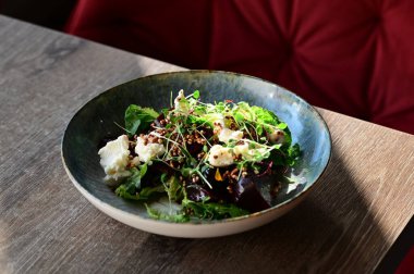 Kavrulmuş pancar, peynir ve taze otlarla dolu bir salatanın yakın plan görüntüsü, ahşap bir masadaki bir restoranda bir tabakta servis ediliyor. Canlı renklere ve taze malzemelere sahip sağlıklı bir mevsimlik yemek, modern gastronomi için mükemmel, sağlıklı beslenme.