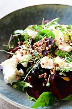 Kavrulmuş pancar, peynir ve taze otlarla dolu bir salatanın yakın plan görüntüsü, ahşap bir masadaki bir restoranda bir tabakta servis ediliyor. Canlı renklere ve taze malzemelere sahip sağlıklı bir mevsimlik yemek, modern gastronomi için mükemmel, sağlıklı beslenme.