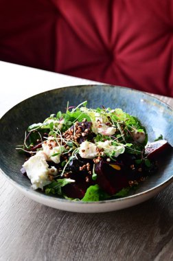 Kavrulmuş pancar, peynir ve taze otlarla dolu bir salatanın yakın plan görüntüsü, ahşap bir masadaki bir restoranda bir tabakta servis ediliyor. Canlı renklere ve taze malzemelere sahip sağlıklı bir mevsimlik yemek, modern gastronomi için mükemmel, sağlıklı beslenme.
