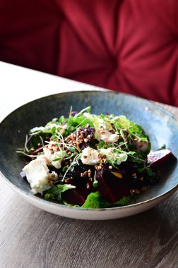 Kavrulmuş pancar, peynir ve taze otlarla dolu bir salatanın yakın plan görüntüsü, ahşap bir masadaki bir restoranda bir tabakta servis ediliyor. Canlı renklere ve taze malzemelere sahip sağlıklı bir mevsimlik yemek, modern gastronomi için mükemmel, sağlıklı beslenme.