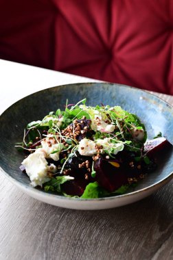 Kavrulmuş pancar, peynir ve taze otlarla dolu bir salatanın yakın plan görüntüsü, ahşap bir masadaki bir restoranda bir tabakta servis ediliyor. Canlı renklere ve taze malzemelere sahip sağlıklı bir mevsimlik yemek, modern gastronomi için mükemmel, sağlıklı beslenme.