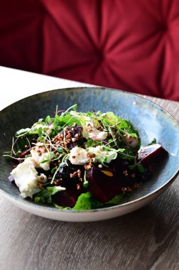 Kavrulmuş pancar, peynir ve taze otlarla dolu bir salatanın yakın plan görüntüsü, ahşap bir masadaki bir restoranda bir tabakta servis ediliyor. Canlı renklere ve taze malzemelere sahip sağlıklı bir mevsimlik yemek, modern gastronomi için mükemmel, sağlıklı beslenme.