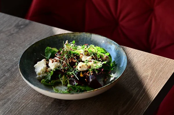Kavrulmuş pancar, peynir ve taze otlarla dolu bir salatanın yakın plan görüntüsü, ahşap bir masadaki bir restoranda bir tabakta servis ediliyor. Canlı renklere ve taze malzemelere sahip sağlıklı bir mevsimlik yemek, modern gastronomi için mükemmel, sağlıklı beslenme.