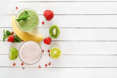 Taze yeşil smoothies ve çilek beyaz tahtalar üzerinde tropikal meyve ile cam bardaklarda bir milkshake. Görünümü üst. Sağlıklı bir diyet kavramı. Kopya alanı