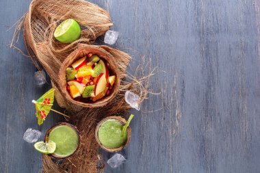 Meyve salatası elma, kivi, portakal ve nar yarısı Hindistan cevizi buzlu ve limonlu taze yeşil smoothies ve nane Hindistan cevizi kabuğu. Üstten görünüm. Sağlıklı bir diyet kavramı. Kopya alanı