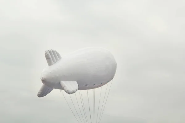 White inflatable dirigible with a place for a logo on a background of a gray sky with clouds. Copy space