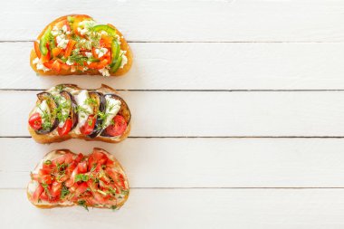 Bruschetta taze domates ve peynir, patlıcan ve mozzarella peyniri, tatlı biber ve beyaz tahtalar üzerinde keçi peyniri. Üstten görünüm. Kopya alanı.