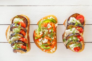 Bruschetta taze domates ve peynir, patlıcan ve mozzarella peyniri, tatlı biber ve keçi peyniri siyah bir arka plan ile. Üstten görünüm.