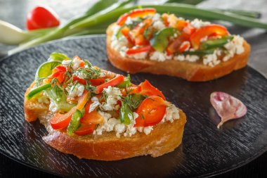 Bruschetta kırmızı tatlı biber ve taze sebze bir arka plan üzerinde siyah bir tablo üzerinde keçi peyniri ile. Yakın çekim