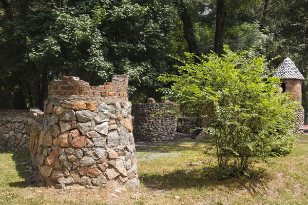 dilapidated stone tower and a brick wall of a children's play complex in the style of a medieval castle in the park