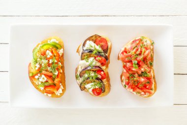 Bruschetta taze domates ve peynir, patlıcan ve mozzarella peyniri, tatlı biber ve beyaz bir plaka üzerinde keçi peyniri. Üstten görünüm