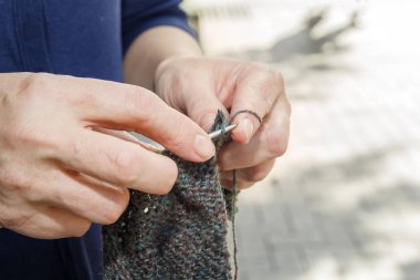 kadın güneşli bir günde dışında sokakta yün örgü iğne üzerinde dokuma kumaşlar. Yakın çekim. Kopya alanı.