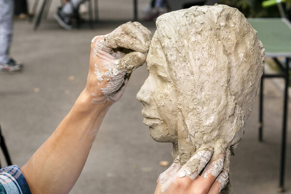 sculptor creates a bust and puts his hands clay on the skeleton of the sculpture. Close-up