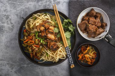 Çin Eriştesi mantar ile bir tavada, sebze ve otlar kızarmış et gri masada vardır. Üstten görünüm