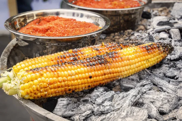 Fried Mexican corn with red pepper is turned on hot coals. Fast food on the street. Close-up